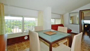 A dining area with a glass table, four chairs, a red sofa, and large windows with curtains.
