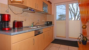 Eine Küche mit Holzausstattung, einer Mikrowelle, einer roten Kaffeemaschine und einem Fenster mit Vorhängen.
