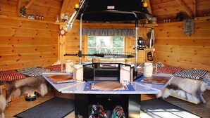 Ein gemütliches Blockhaus-Interieur mit einem zentralen Holztisch, einem schwarzen Grill und zwei Hunden auf dem Boden.