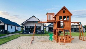 A playground with a wooden playhouse and swings on a sandy area. - Summer House in Jaroslawiec Near Beach & Pool (Postomino)