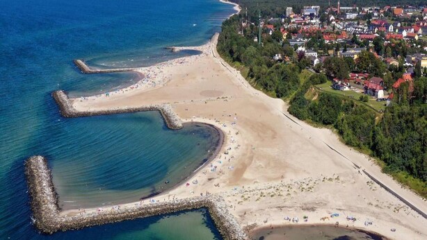 An aerial view of a coastal town with a sandy beach, a pier, and residential buildings. - Summer House in Jaroslawiec Near Beach & Pool (Postomino)
