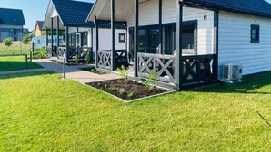 A row of white cabins with dark roofs, each featuring a porch and a small garden area. - Summer House in Jaroslawiec Near Beach & Pool (Postomino)