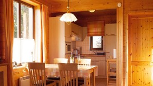A cozy wooden interior with a dining table, chairs, a hanging light fixture, and a kitchen area with cabinets and appliances. - Doppelhaushalfte in Hasselfelde (Oberharz am Brocken)