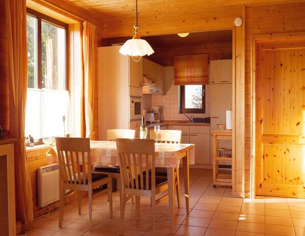 A cozy wooden interior with a dining table, chairs, a hanging light fixture, and a kitchen area with cabinets and appliances.