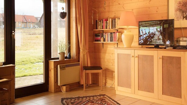 A cozy cabin interior with a wooden floor, a bookshelf, a television, and a window with curtains. - Doppelhaushalfte in Hasselfelde (Oberharz am Brocken)