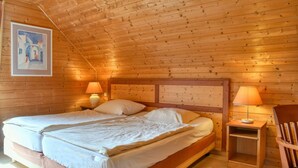 A wooden cabin bedroom with a bed, two bedside lamps, a chair, and a painting on the wall. - Doppelhaushalfte in Hasselfelde (Oberharz am Brocken)