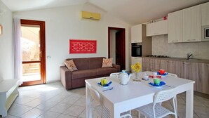 A modern kitchen with white cabinets, a dining table with chairs, a sofa, and a red decorative wall piece. - Terraced House in Costa Rei With Garden (Muravera)