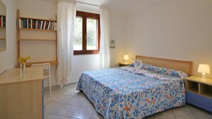 A bedroom with a bed, bedside tables, a desk, a chair, a window, and a bookshelf. - Terraced House in Costa Rei With Garden (Muravera)