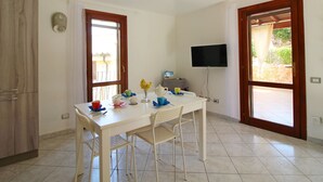 A small, clean room with a white table, two chairs, a TV, and a window. - Terraced House in Costa Rei With Garden (Muravera)