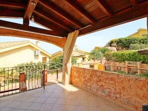 Un balcone coperto con pavimento piastrellato, ringhiera in metallo e vista su edifici residenziali e vegetazione.