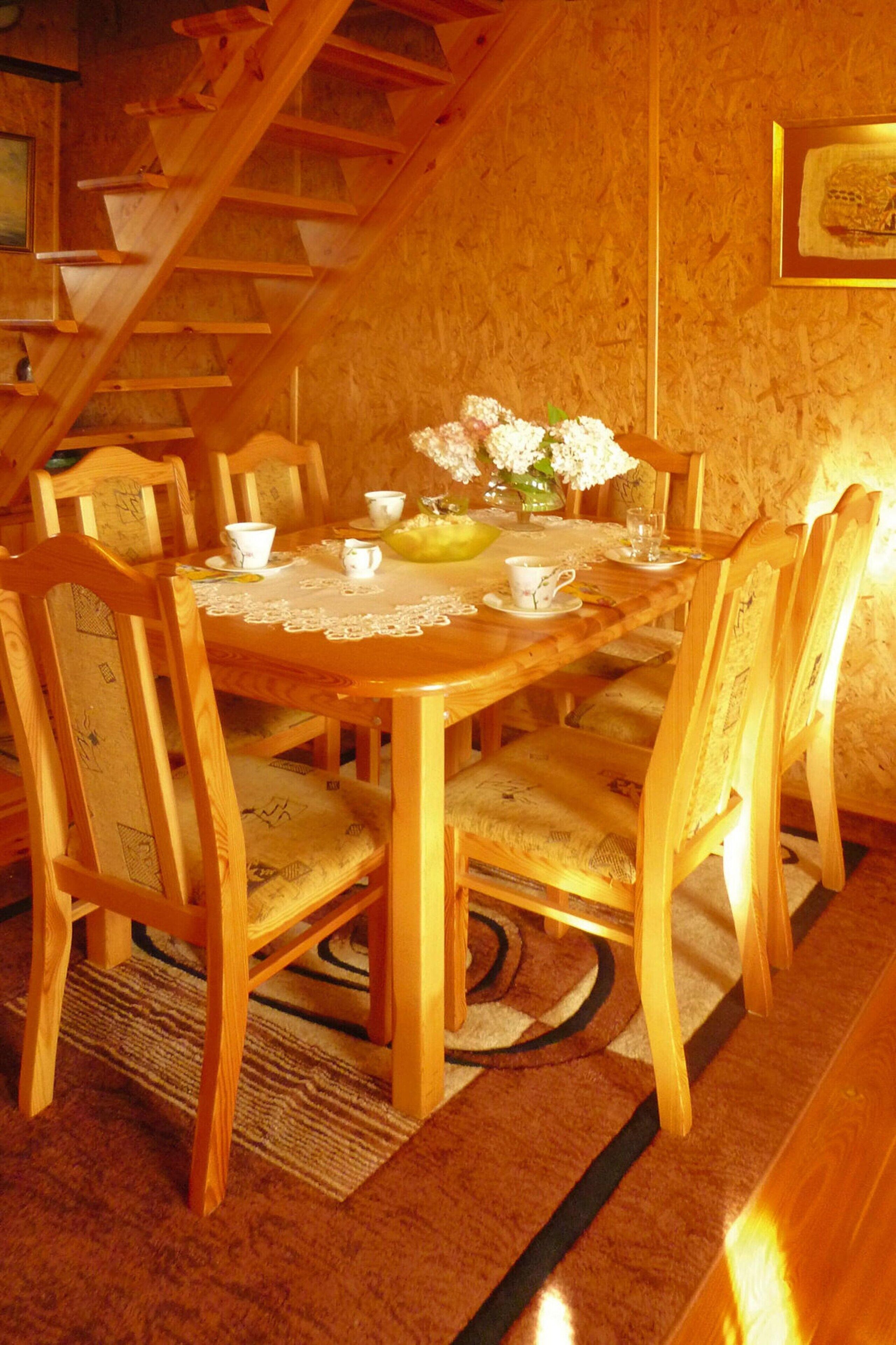 Una mesa de comedor de madera con sillas, mantel de encaje y un florero con flores.
