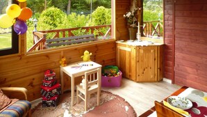 L’intérieur d’un chalet en bois, avec une grande fenêtre, une petite table avec des jouets, une chaise et un tapis coloré.
