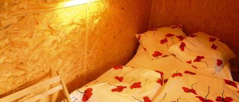 Una habitación con una cama cubierta con ropa de cama blanca y motivos florales rojos, un cabecero de madera y una lámpara de pared.
