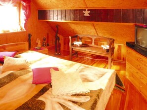 A cozy attic bedroom with a wooden bed, a bench, a television, and a window with curtains. - House Near Lake Zawiat and Baltic Sea (Wejherowo)