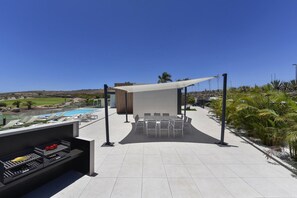 Ein Außenbereich mit Terrasse, Blick auf einen Pool, einer Grillstation und einer Sitzgruppe.