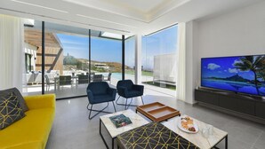 A modern living room with a yellow sofa, two blue armchairs, a marble coffee table, and a large flat-screen TV.