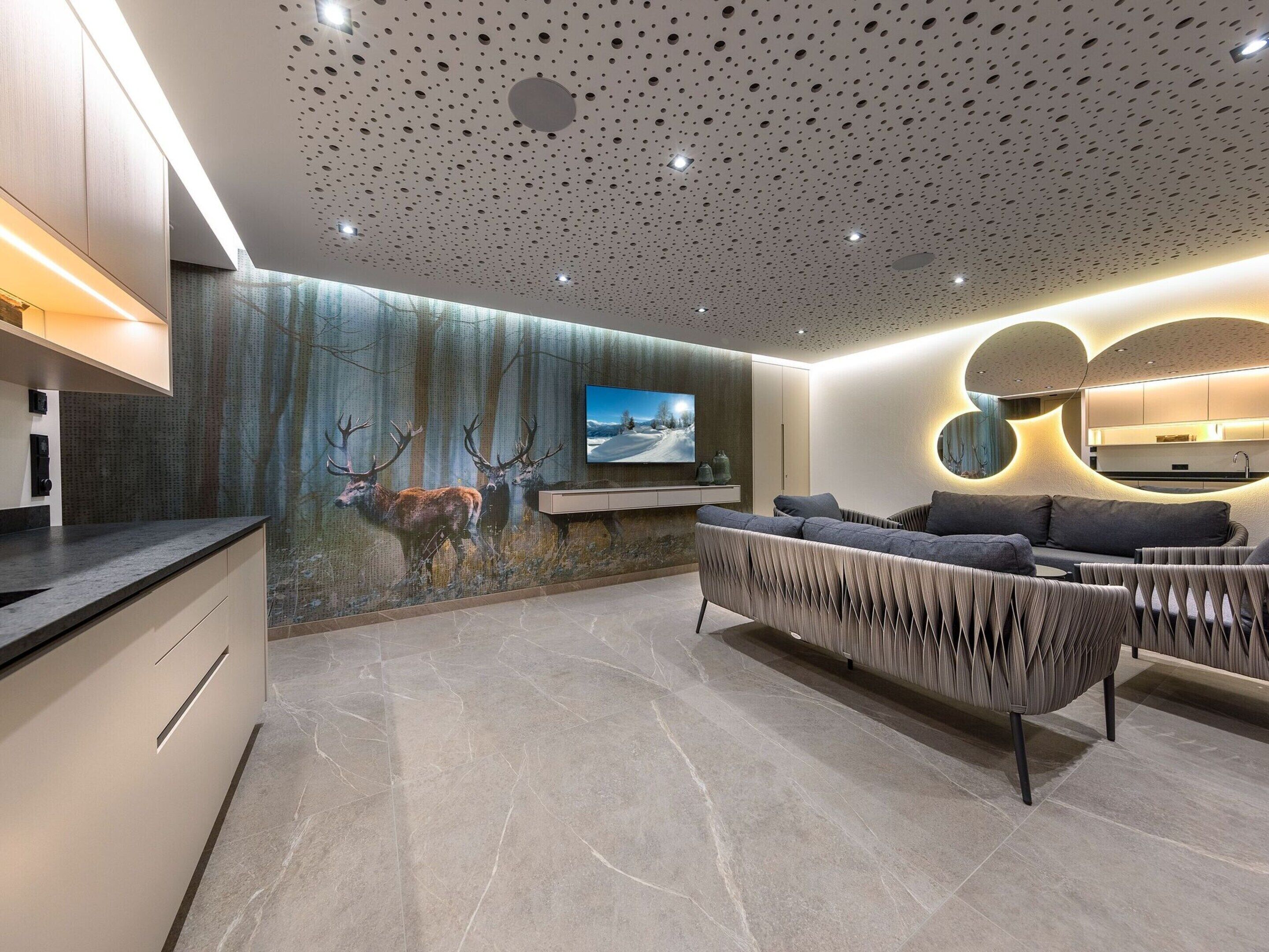 A modern living room with a large TV, a sofa, and a wall mural of deer.