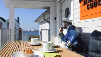 A wooden deck with a table set for two, a muffin, and a cup. A statue of a sailor is visible on the right.