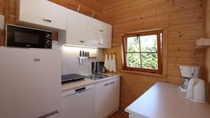 A compact kitchen with white cabinets, a microwave, a coffee maker, and a window with a view of greenery. - Bungalow in Miedzyzdroje Near Baltic Beach (Miedzyzdroje)