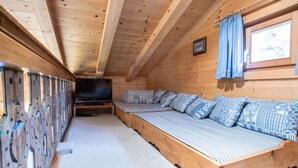 A wooden cabin with a long, narrow room featuring a built-in bench with patterned cushions, a television, and a window with curtains. - Chalet in Austria Near Ski Lift & Forest (Wald im Pinzgau)