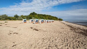 Ein Strand mit Reihen von Strandhütten mit Streifenmarkisen, einem Sandstrand und einem bewaldeten Hügel im Hintergrund.