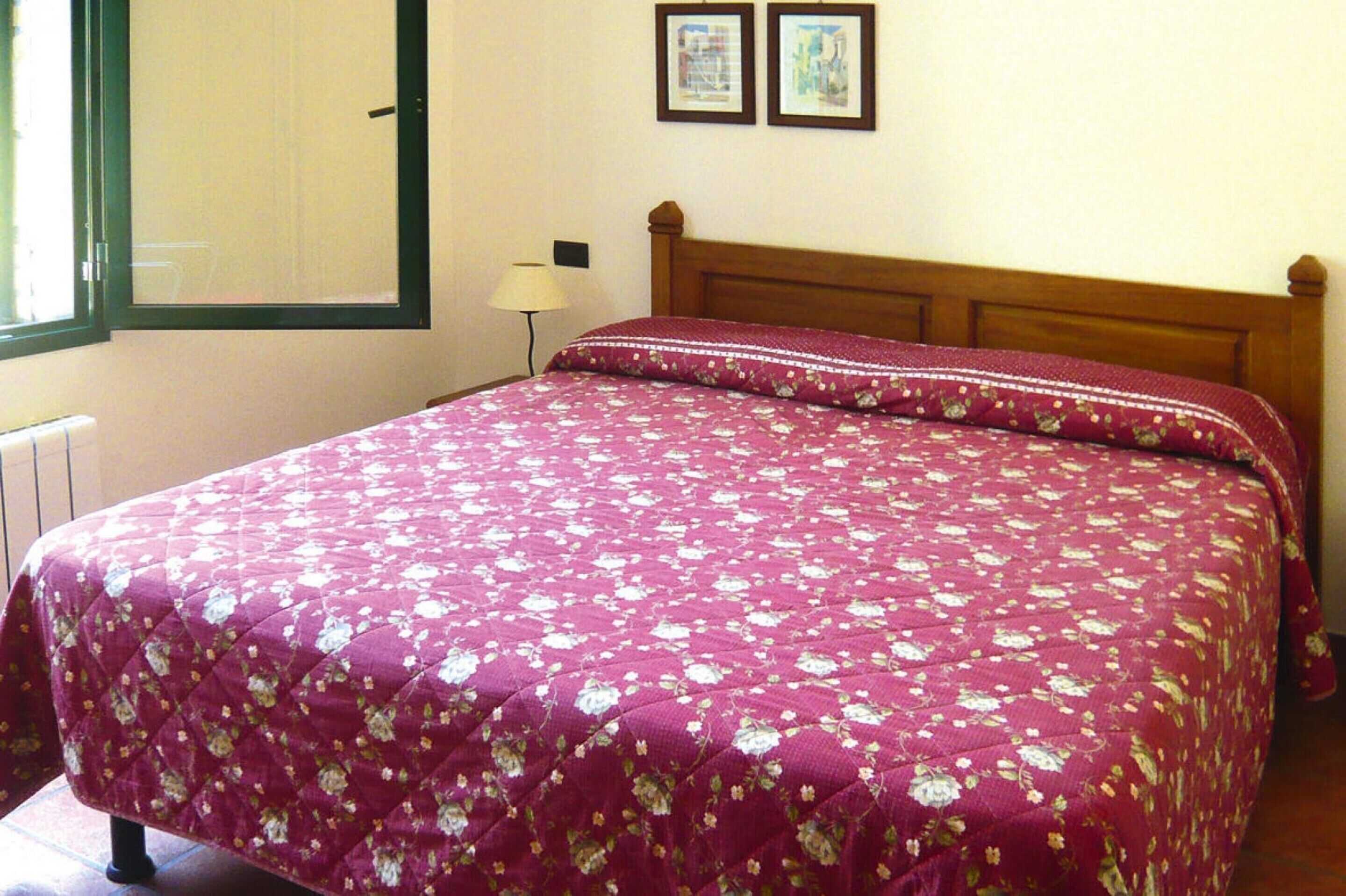 A bed with a floral bedspread, a wooden headboard, and two framed pictures on the wall.