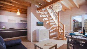 Una cocina moderna con armarios blancos, una escalera de madera y una zona de comedor con mesa y sillas.