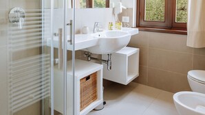 A modern bathroom with a white sink, mirror, and toilet. There is a window with a view of greenery outside. - Il Limone Lake View at Nautic Resort San Carlo (Gargnano)