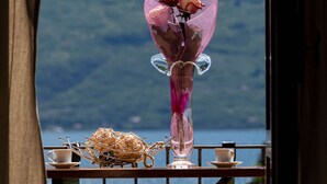 A table with a vase of pink roses, a decorative glass object, and two cups, set against a scenic mountain backdrop. - Il Limone Lake View at Nautic Resort San Carlo (Gargnano)
