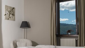 A neatly made bed with a white duvet, a lamp, a window with curtains, and a wall-mounted picture. - Il Limone Lake View at Nautic Resort San Carlo (Gargnano)