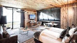 A modern hotel room with a wooden ceiling, a large bed, a sofa, a dining table, and a TV mounted on the wall. - Apartment in Kaltenbach With Ski-in/ski-out (Kaltenbach)