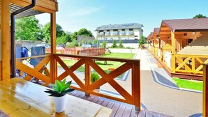Una terraza de madera con una mesa y sillas, con vistas a una hilera de cabañas de madera y un edificio con techo inclinado.