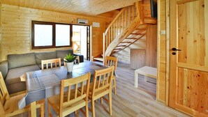Interior de una cabaña de madera con comedor, sofá, escalera y una amplia puerta de madera.