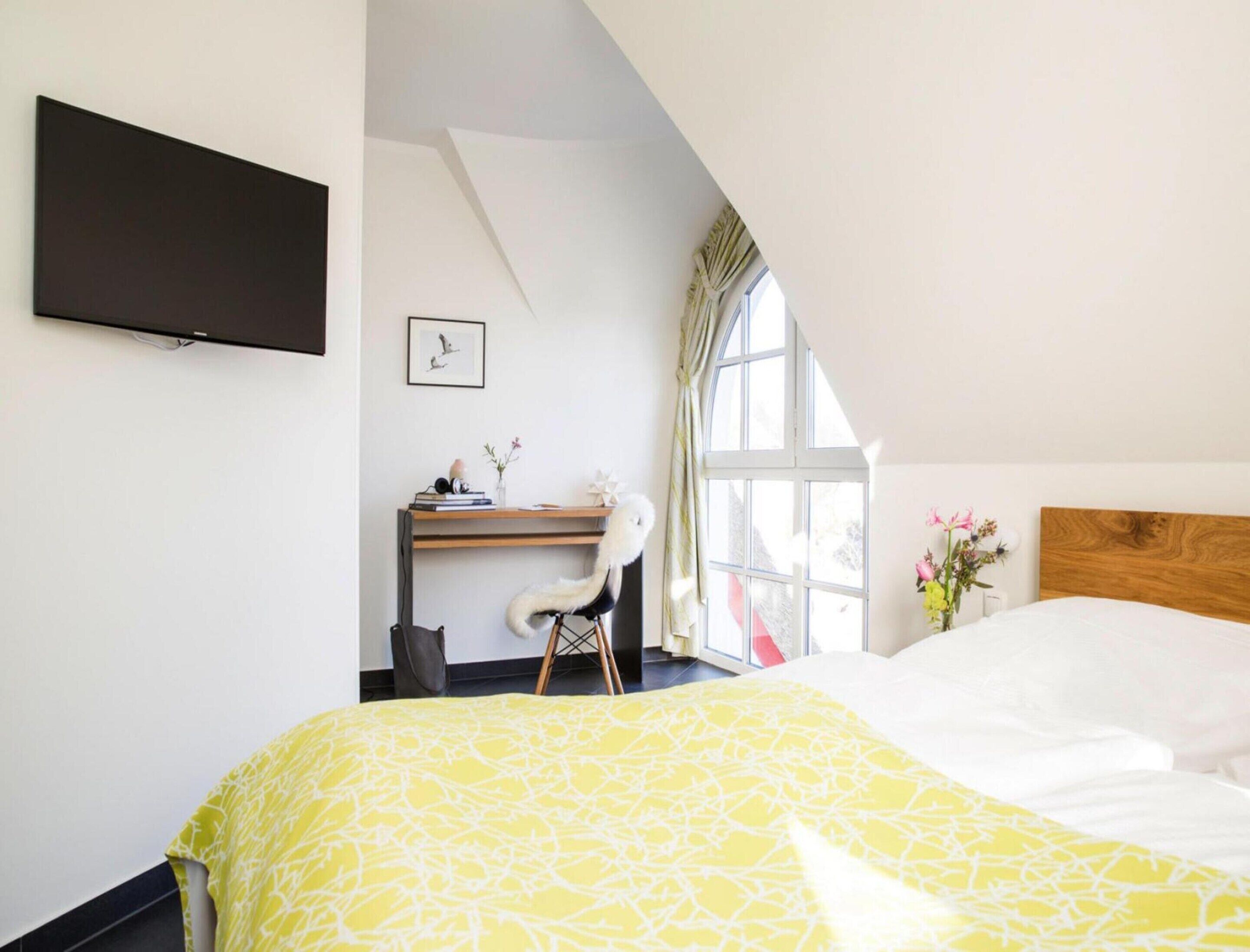 Une chambre à coucher avec un lit, un bureau, une chaise, un téléviseur et une fenêtre avec des rideaux.