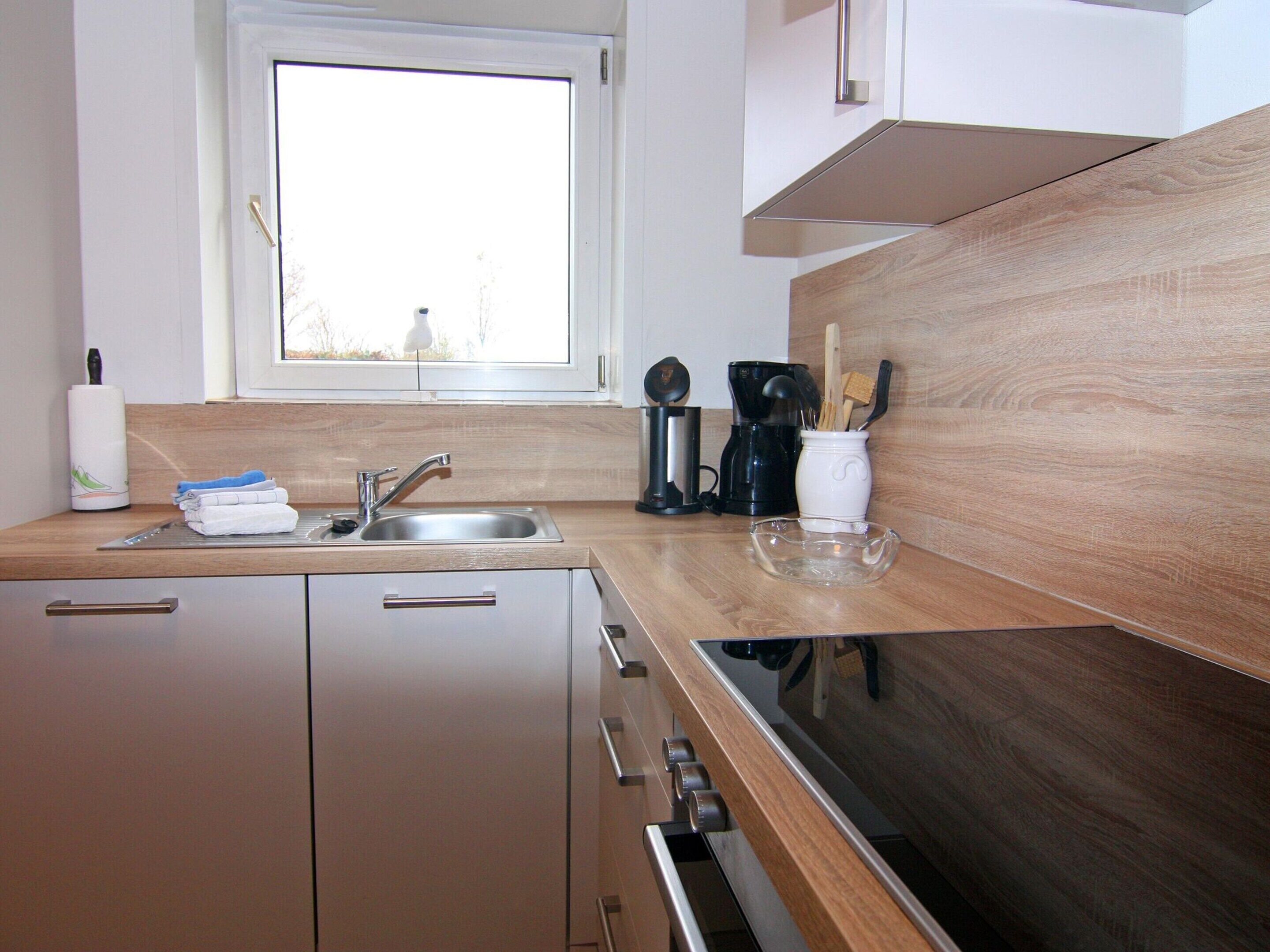 A modern kitchen with a stainless steel sink, wooden countertop, and a window above the sink.