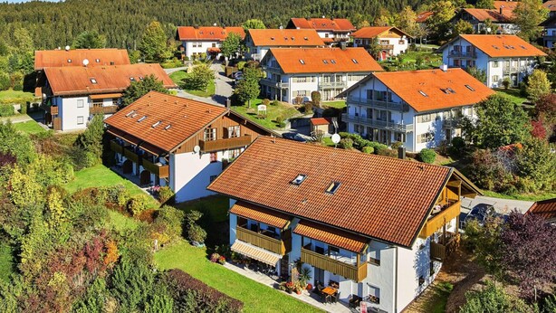 Ett bostadsområde med hus som har röda tegeltak och vita väggar, omgivet av grönska och kullar.