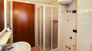 Un baño con puerta de madera, lavamanos blanco, cabina de ducha de vidrio y un calentador fijado a la pared.