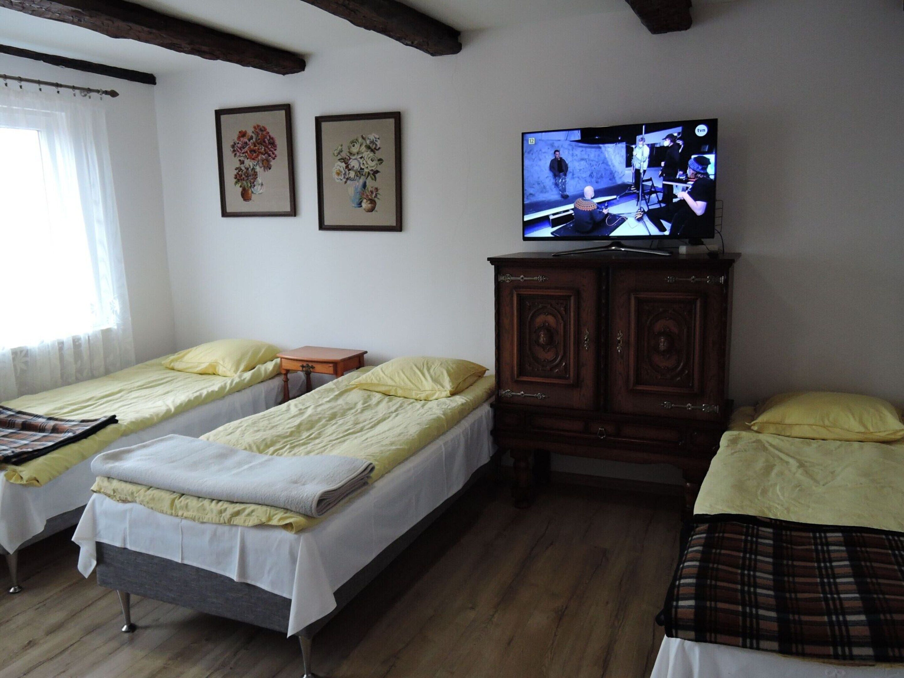 A room with two single beds, a wooden cabinet, a television, and two framed floral paintings on the wall.