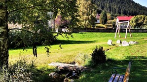 Un'area verde con prato, una panchina di legno, altalene e un piccolo ruscello.