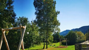 Un’altalena in legno in un parco, con cielo sereno e montagne sullo sfondo.