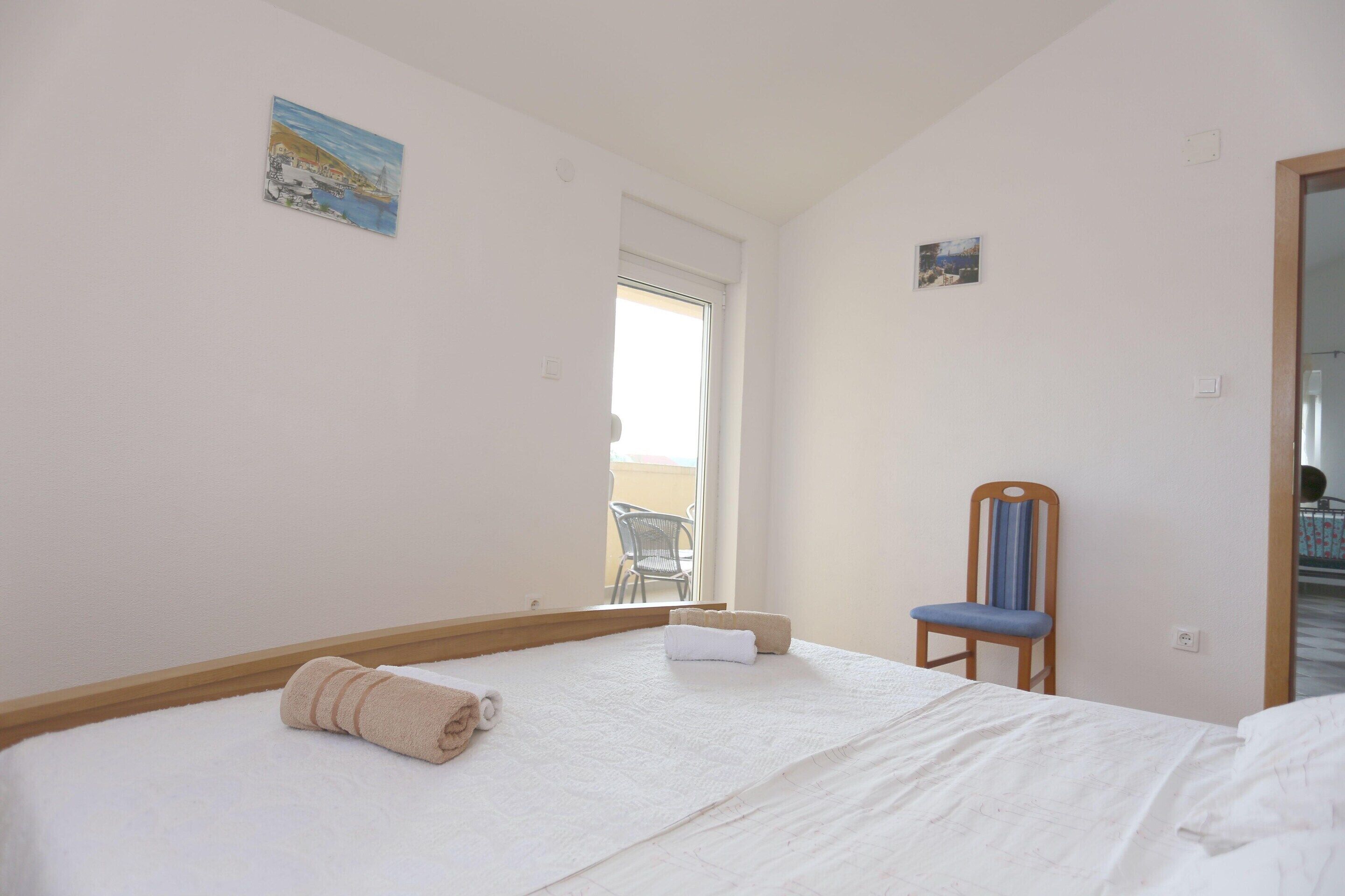 A bedroom with a bed, a chair, a small painting, and a window.