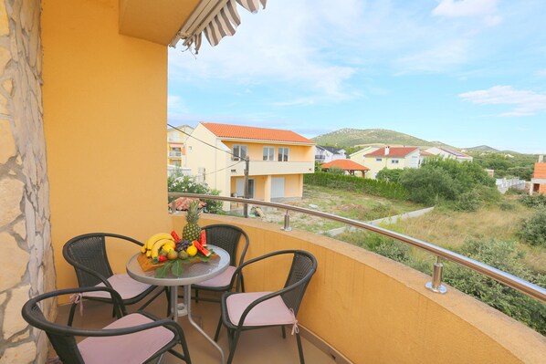 A balcony with wicker chairs, a table with fruit, and a view of houses and greenery. - Apartment in Kakma Near Biograd Beaches (Polaca)
