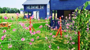 A blue house with a porch and a garden with pink flowers. - Holiday Home, Nowe Warpno for 6 Persons (Nowe Warpno)