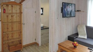 A wooden cabinet with multiple shelves, a television mounted on the wall, a sofa with a cushion, and a wooden coffee table with fruit. - Holiday Home, Nowe Warpno for 6 Persons (Nowe Warpno)