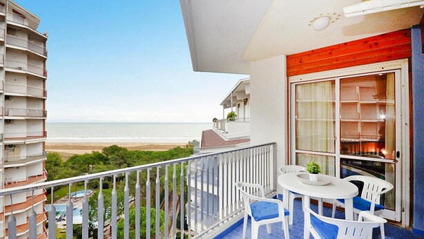 A balcony with a view of the beach, a dining table with chairs, and a large window with curtains. - Residence Marco Polo, Lignano Sabbiadoro (Lignano Sabbiadoro)
