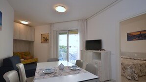 A compact living space with a dining table, chairs, a sofa, a TV, and a balcony with a view. - Residence Marco Polo, Lignano Sabbiadoro (Lignano Sabbiadoro)