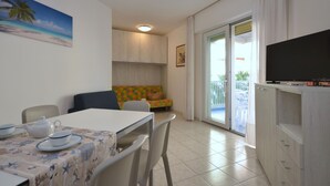 A dining area with a table set for two, a sofa, and a television on a cabinet. - Residence Marco Polo, Lignano Sabbiadoro (Lignano Sabbiadoro)