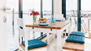 Ein Essbereich mit einem Tisch für zwei Personen, einer Blumenvase und Blick auf das Wasser.