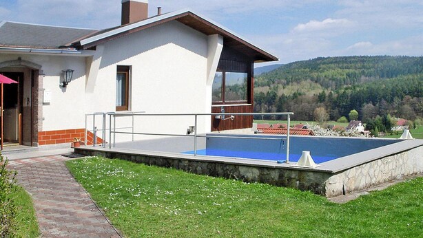 Ein Haus mit Pool, einem Ziegelweg und Blick auf einen bewaldeten Hügel.