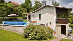 Ein zweigeschossiges Haus mit Swimmingpool, Steinmauer und Garten mit rosa Blumen.